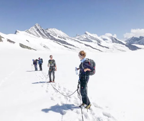 Group of people roped together, hiking on a snowy mountain with backpacks and trekking poles.