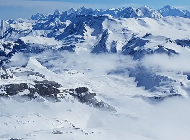 Snow-covered mountain range with peaks and valleys under a clear blue sky.