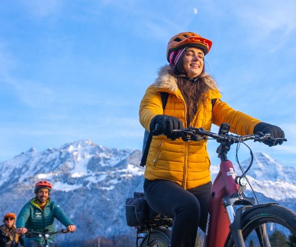 People biking with helmets and winter jackets in a snowy mountain landscape.
