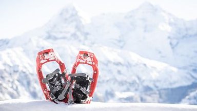 Rote Schneeschuhe im Schnee vor verschneiten Bergen in der Schweiz.