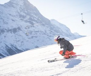 Person skiing with a helmet is going down a snow-covered slope, mountains in the background.