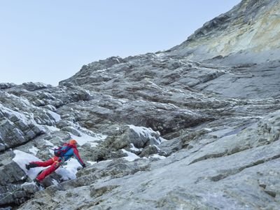 Climber with helmet and climbing harness on rocky mountain terrain with snow.