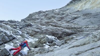Climber with helmet and climbing harness on rocky mountain terrain with snow.