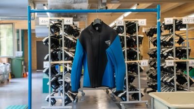 Neoprenanzug in Blau und Schwarz hängt an einem blauen Metallgestell in einem Raum mit Regalen voller weiterer Anzüge.