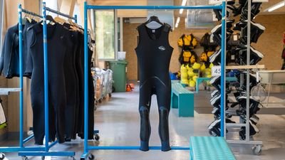 Neoprenanzüge hängen in einem Verleihraum mit weiteren Ausrüstungsgegenständen für Wassersport.