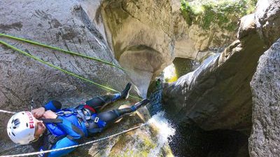 Person beim Canyoning mit Helm und Klettergurt, der einen felsigen Wasserfall in einer engen Schlucht hinabsteigt.