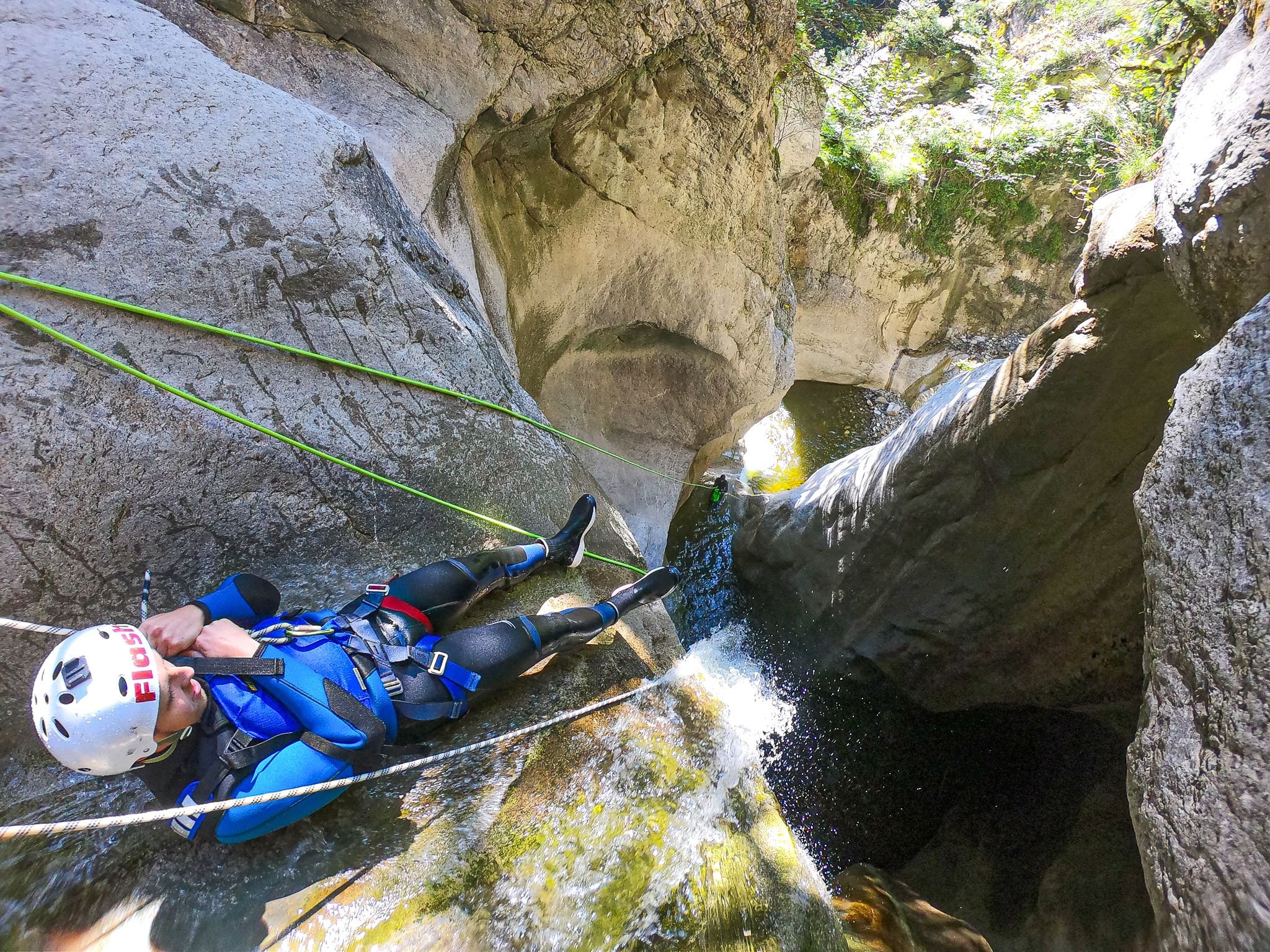 Person beim Canyoning mit Helm und Klettergurt, der einen felsigen Wasserfall in einer engen Schlucht hinabsteigt.