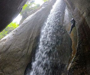 Person, der neben einem Wasserfall in einer Schlucht abseilt, trägt einen Helm und ein Gurtzeug.