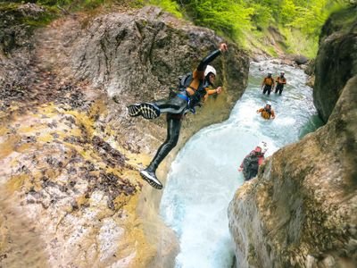 Person in Neoprenanzug und Helm springt in den Canyon-Pool; andere in Helmen und Ausrüstung beobachten vom Wasser aus.