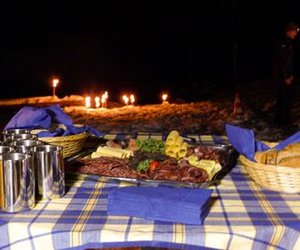 Table with food and drinks outdoors, surrounded by torches in the snow at night.