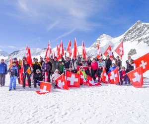 Group of people with Swiss flags in the snow, surrounded by snow-covered mountains.