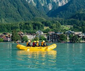 Group during Family Rafting on the turquoise blue Lake Brienz, picturesque village and mountains in the background.