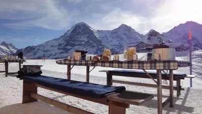 Tables with food and drinks in the snow in front of a mountain backdrop, no people visible.