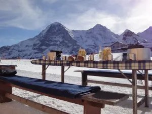 Tables with food and drinks in the snow in front of a mountain backdrop, no people visible.