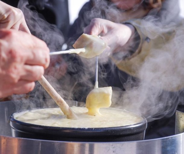 People are dipping bread into a pot of melted cheese outdoors in cool weather.