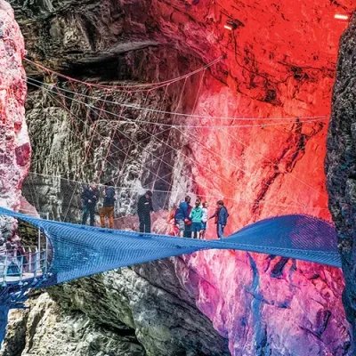 Personen auf einem gespannten Netz in einer beleuchteten Schlucht, umgeben von Felswänden.