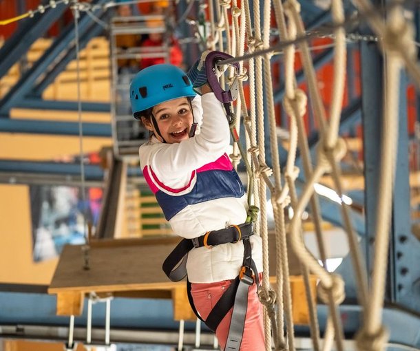 Ein Kind mit Helm und Sicherheitsgurt navigiert einen Seilparcours im Indoor Seilpark Grindelwald