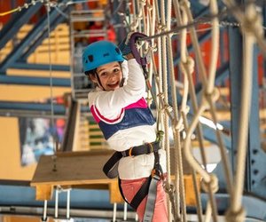 Ein Kind mit Helm und Sicherheitsgurt navigiert einen Seilparcours im Indoor Seilpark Grindelwald