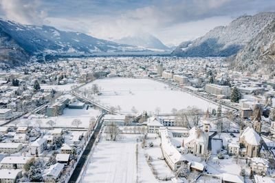 Snowy cityscape with mountains in the background, buildings and streets covered in snow.