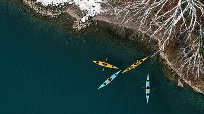 Three kayaks on a lake near a snow-covered coast, people wearing life jackets.