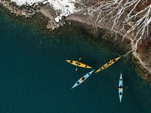 Three kayaks on a lake near a snow-covered coast, people wearing life jackets.