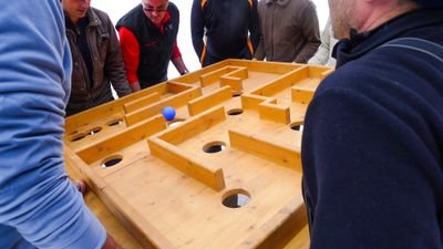 People are balancing a wooden table with a labyrinth and a blue ball.