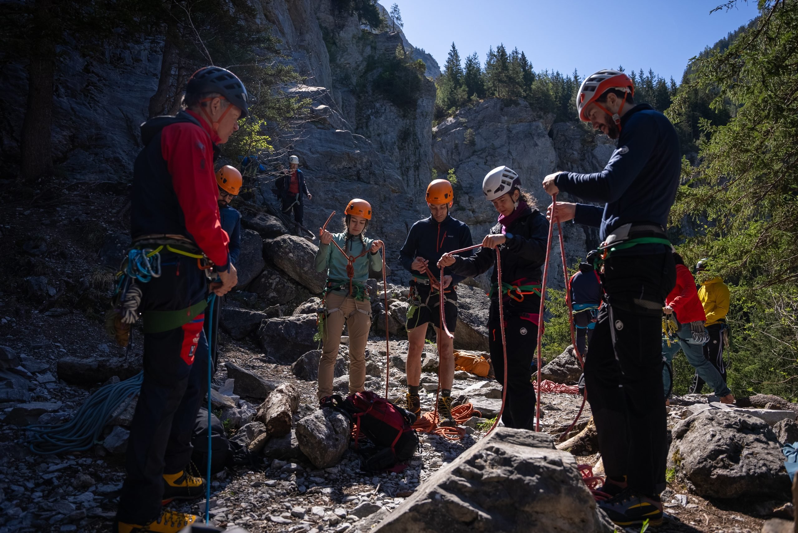 Personen mit Helmen und Klettergurten stehen in felsiger Berglandschaft und bereiten Seile vor.