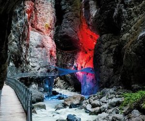 People on an illuminated walkway in a gorge, surrounded by rocks and flowing water.