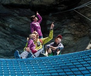 People on blue net in a rocky landscape, wearing casual clothing, pointing upwards.