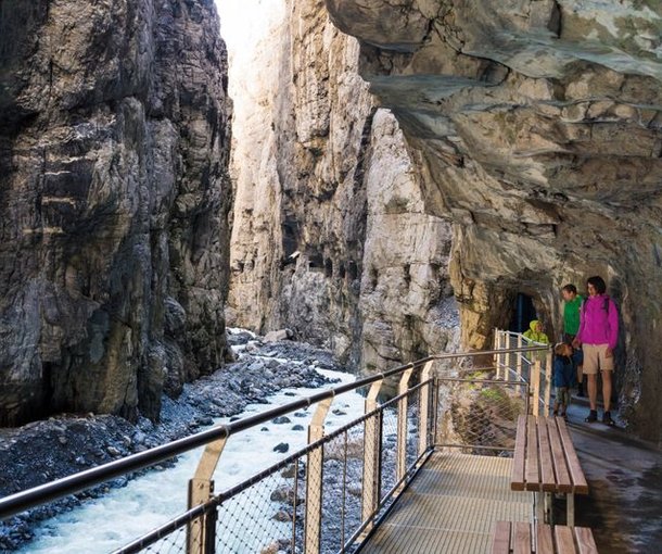 People on a bridge in a gorge, surrounded by rocks and a flowing stream.