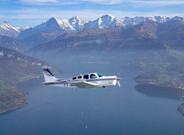 Small airplane flying over a lake with snow-capped mountains in the background.