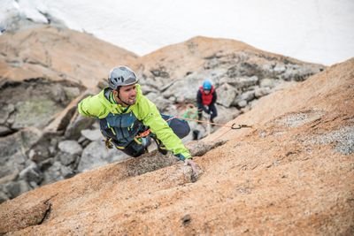 Climber with helmet and rope on rocky mountain wall, second person in the background, snowy environment.