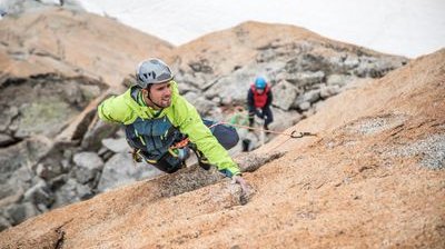 Climber with helmet and rope on rocky mountain wall, second person in the background, snowy environment.