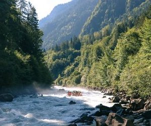 Rafting-Gruppe in Helmen und Rettungswesten navigiert Stromschnellen in einem bewaldeten Flussgebiet in der Jungfrau Region.