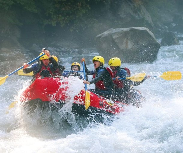 River-Rafting im Wildwasser auf der Lütschine. Teilnehmer tragen Schwimmweste und sitzen paddelnd in einem roten Schlauchboot