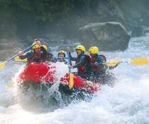 River-Rafting im Wildwasser auf der Lütschine. Teilnehmer tragen Schwimmweste und sitzen paddelnd in einem roten Schlauchboot