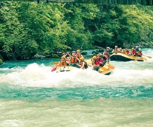 Gruppen beim Rafting auf der Simme, tragen Helme und Rettungswesten, umgeben von grünen Bäumen.