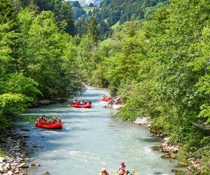 Menschen in Helmen und Rettungswesten, die auf der Simme am river-raften, umgeben von üppig grünen Wäldern und Berge.