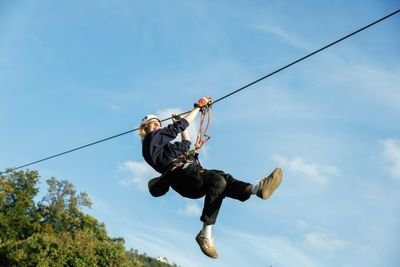 Person beim Seilrutschen mit Helm und Sicherheitsgurt vor blauem Himmel.