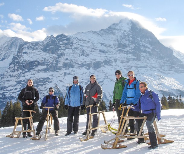 A group of people with sledges on a snow-covered mountain in an alpine setting.