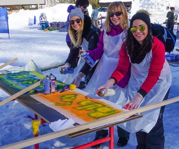 Three people are spraying graffiti on wooden boards in the snow, wearing aprons and gloves.