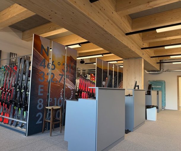 Ski rental with shelves full of ski equipment, wooden beam ceiling, and modern reception desk.
