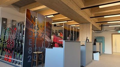 Skiverleih mit Regalen voller Skiausrüstung, Holzbalkendecke und moderner Empfangstheke.