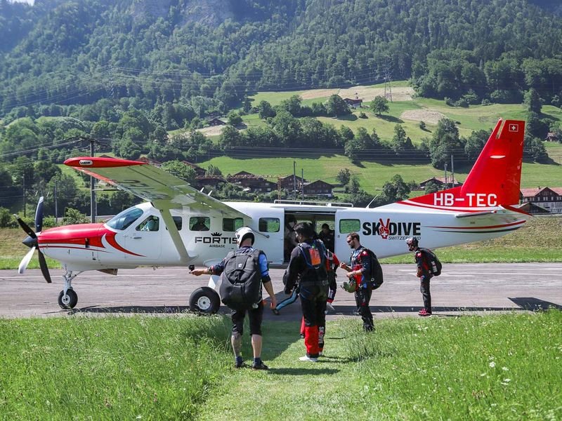 Personen mit Fallschirmausrüstung steigen in ein kleines Flugzeug auf einem Flugfeld in den Bergen ein.