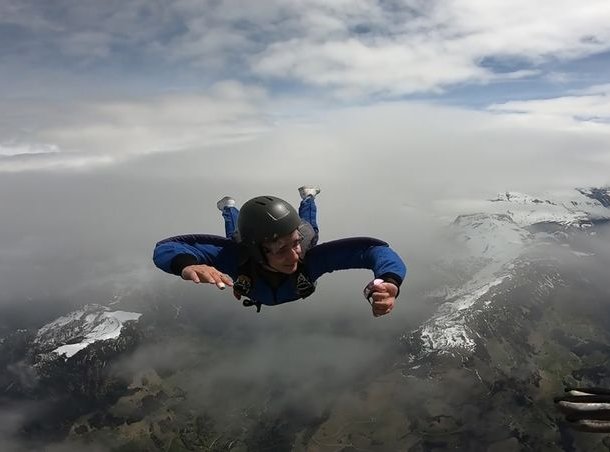 Person in a blue suit and helmet skydiving over snow-covered mountains.