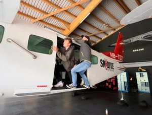 Two people board an airplane in a hangar, visible are airplane doors and wings.