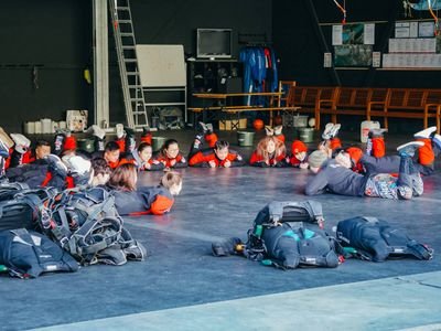 Personen in Overalls liegen auf dem Boden in einer Halle, umgeben von Fallschirmen und Ausrüstung.