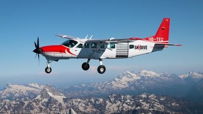 Airplane with Skydive logo flies over snow-covered mountains in Switzerland.
