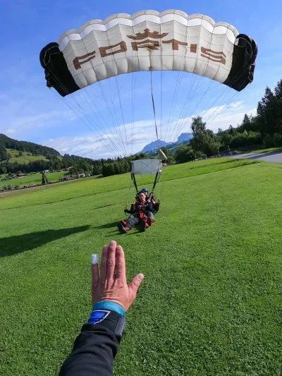 People with parachutes land on a green meadow; a hand in the foreground.