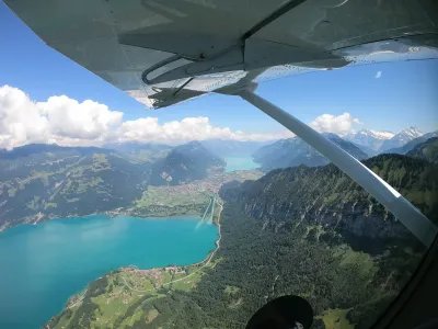 View from an airplane of a turquoise lake surrounded by mountains and forests.
